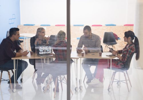 Бизнес-команда стартапа на встрече в современном ярком интерьере офиса, мозговой штурм, работа на ноутбуке и планшетном компьютере